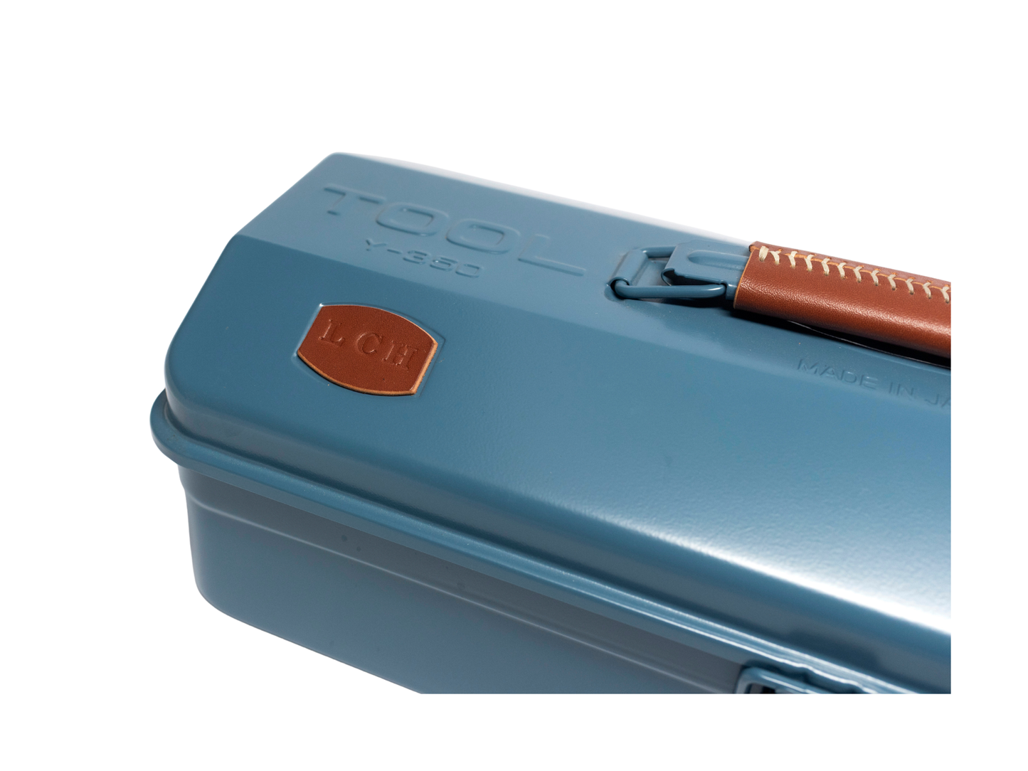 A close-up of a blue metal toolbox lid with a brown leather handle and a small orange shield logo on a white background.
